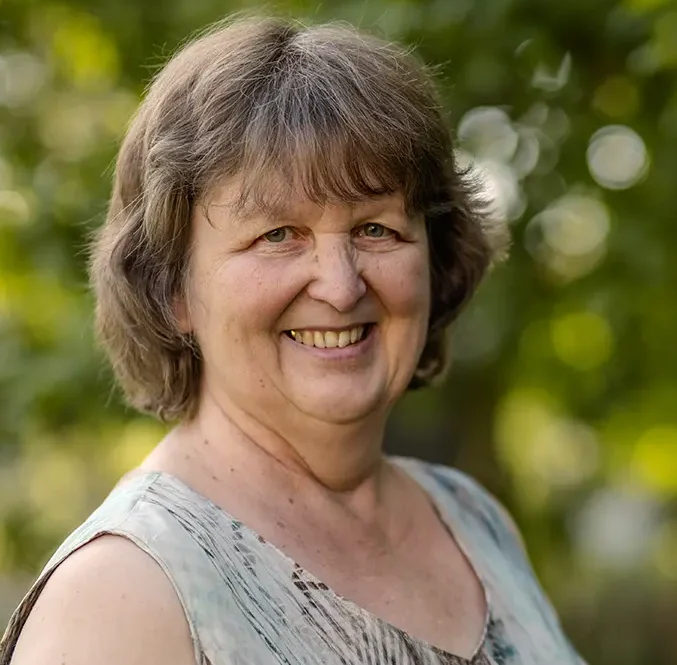 Susanne lächelt im Grünen in die Kamera.